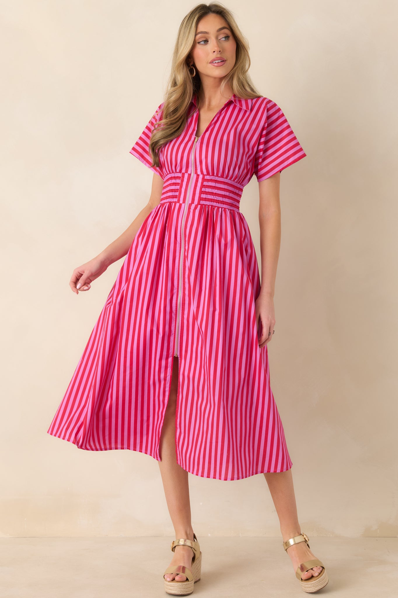 Pink and red vertical striped midi dress with short sleeves, zip-front design, smocked waistband, and a lightweight woven skirt with natural movement.