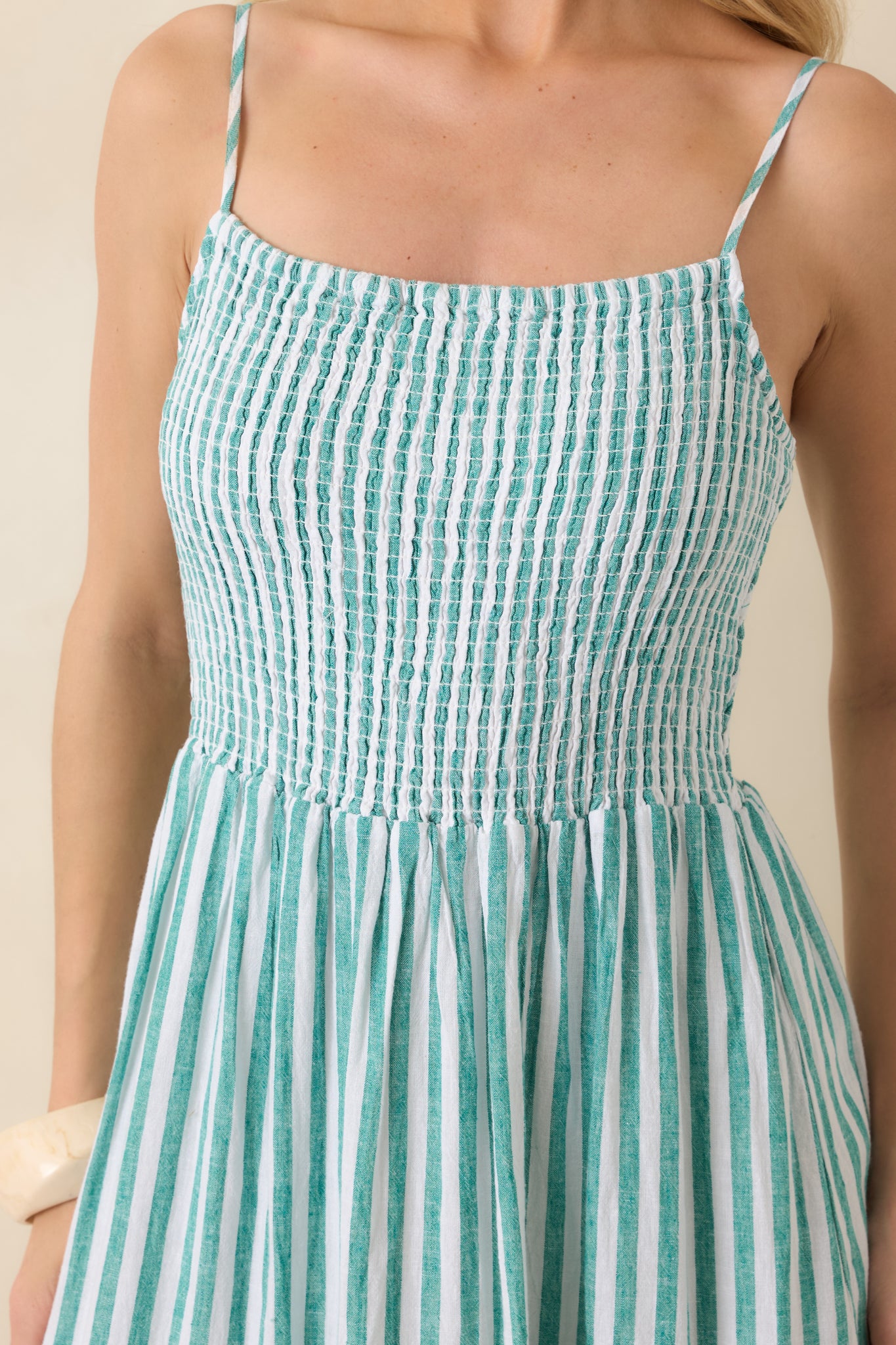 Close-up of smocked bodice and adjustable spaghetti straps on a green-striped linen maxi dress, showing textured fabric.