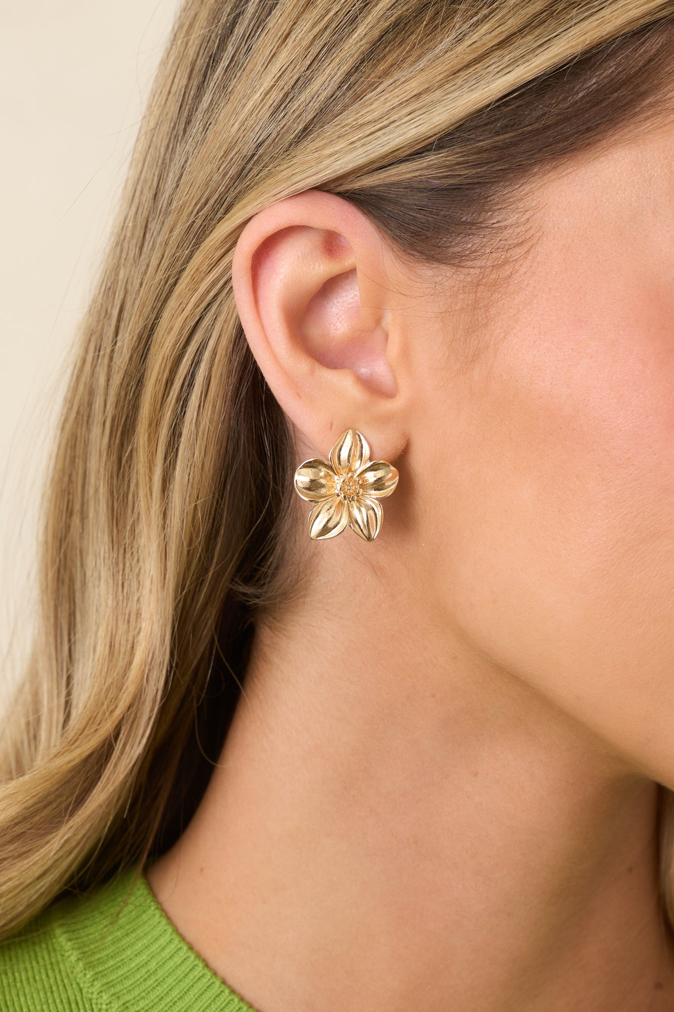 Close-up of glossy gold petals and layered flower shape on statement stud earrings.