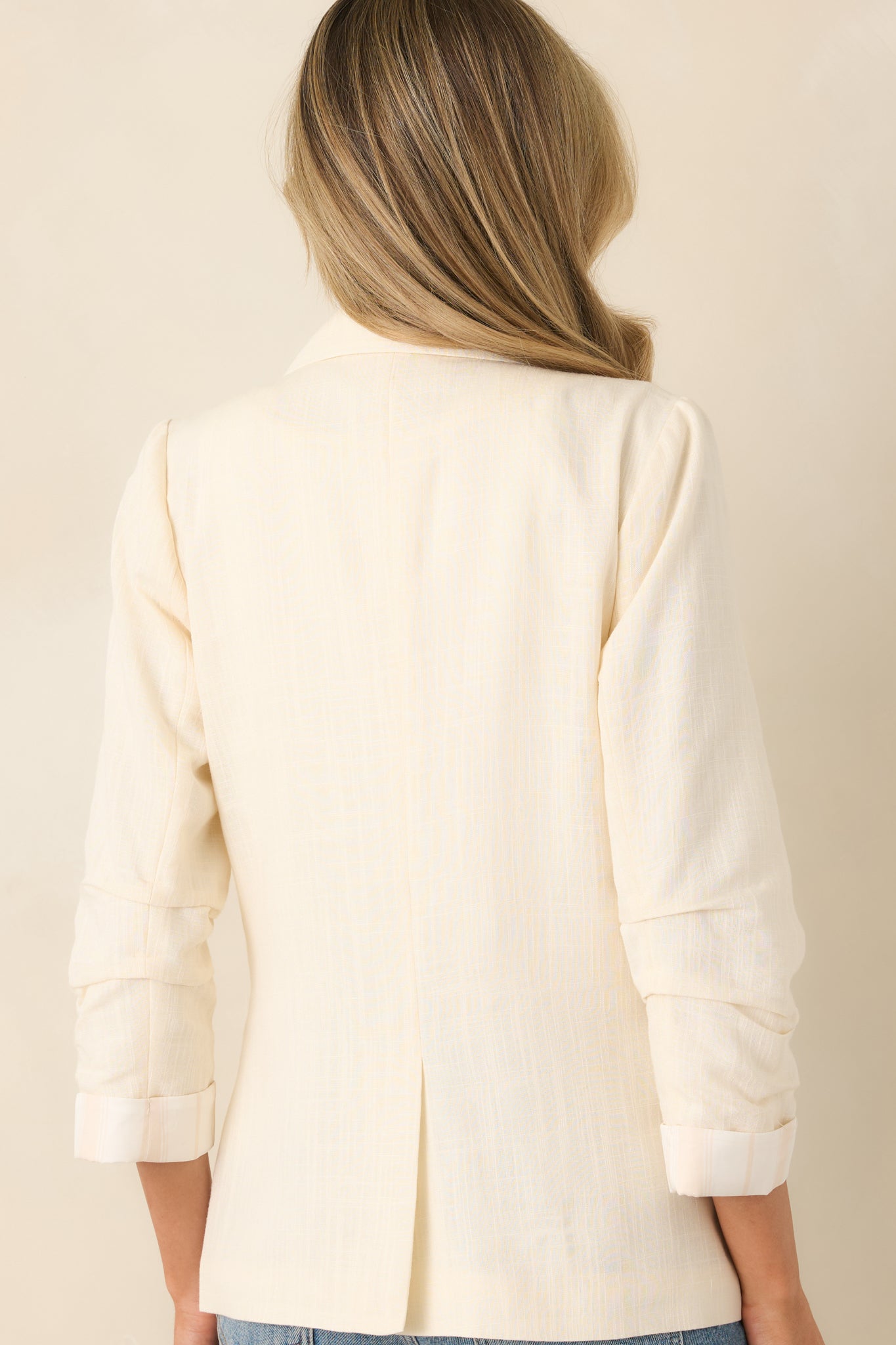 Rear view of the ivory blazer featuring a clean, streamlined silhouette with ruched 3/4 sleeves.