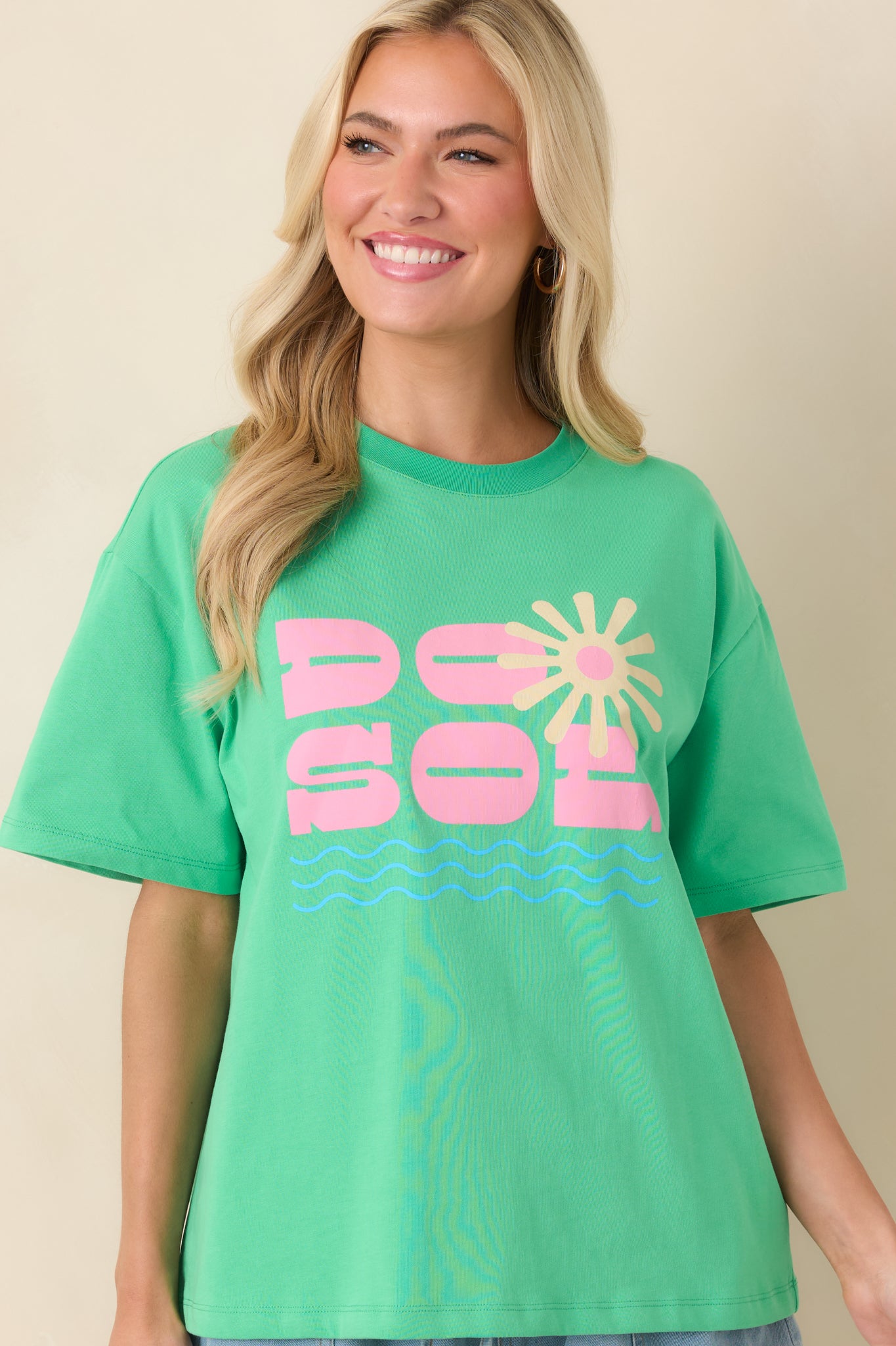 Front graphic detail of the relaxed cotton tee featuring bold pink lettering, a glowing sunburst design, and understated wave accents.