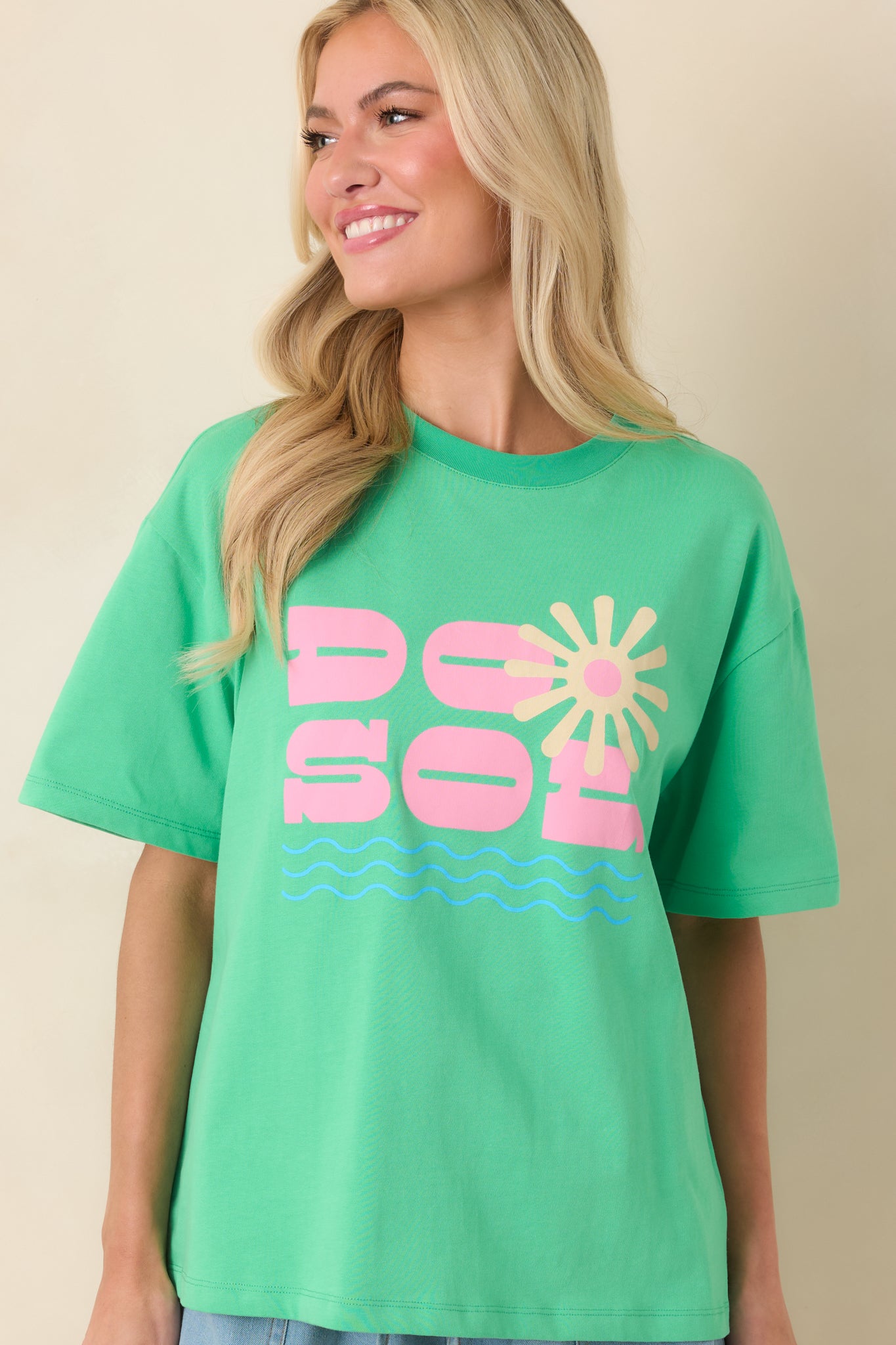 Close front view emphasizing the sunburst motif and pink “DO SOL” text with gentle wave graphics beneath the classic crew neckline.