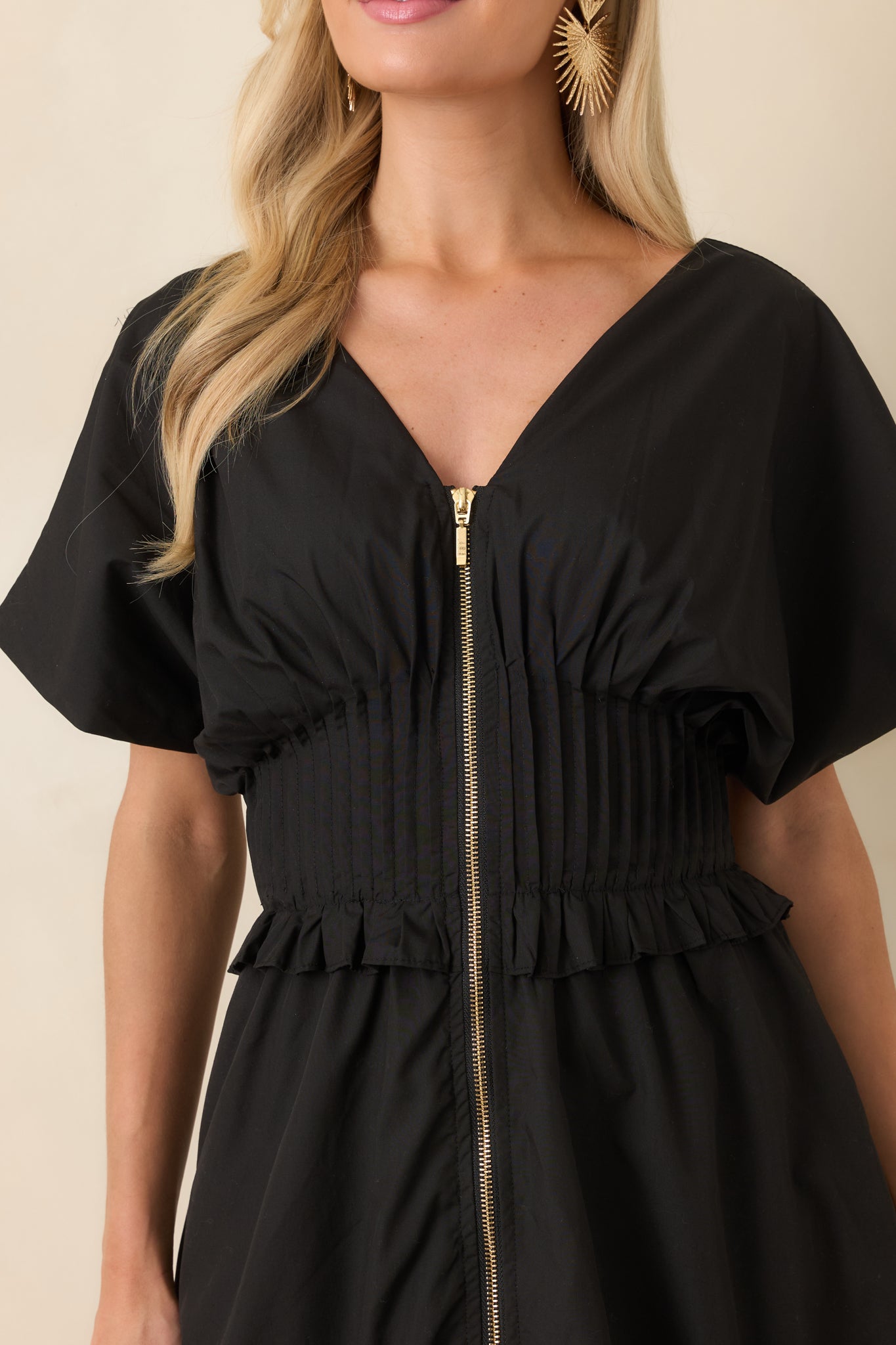 Close look at the smocked waistband with ruffled trim, V-neckline, and front zip closure of the dress.