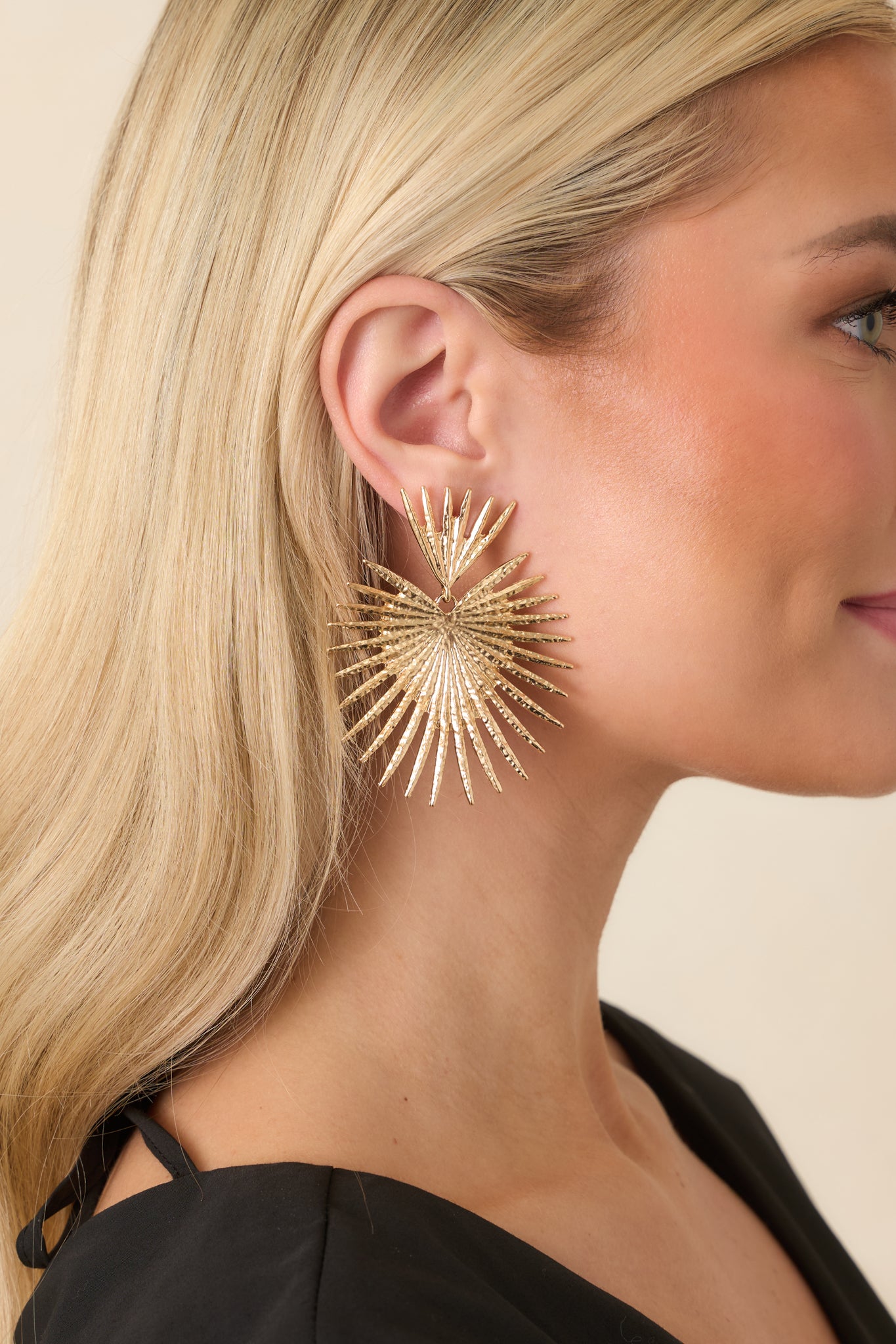 Close view of gold-tone earrings highlighting sculpted fan shape and textured metal finish.