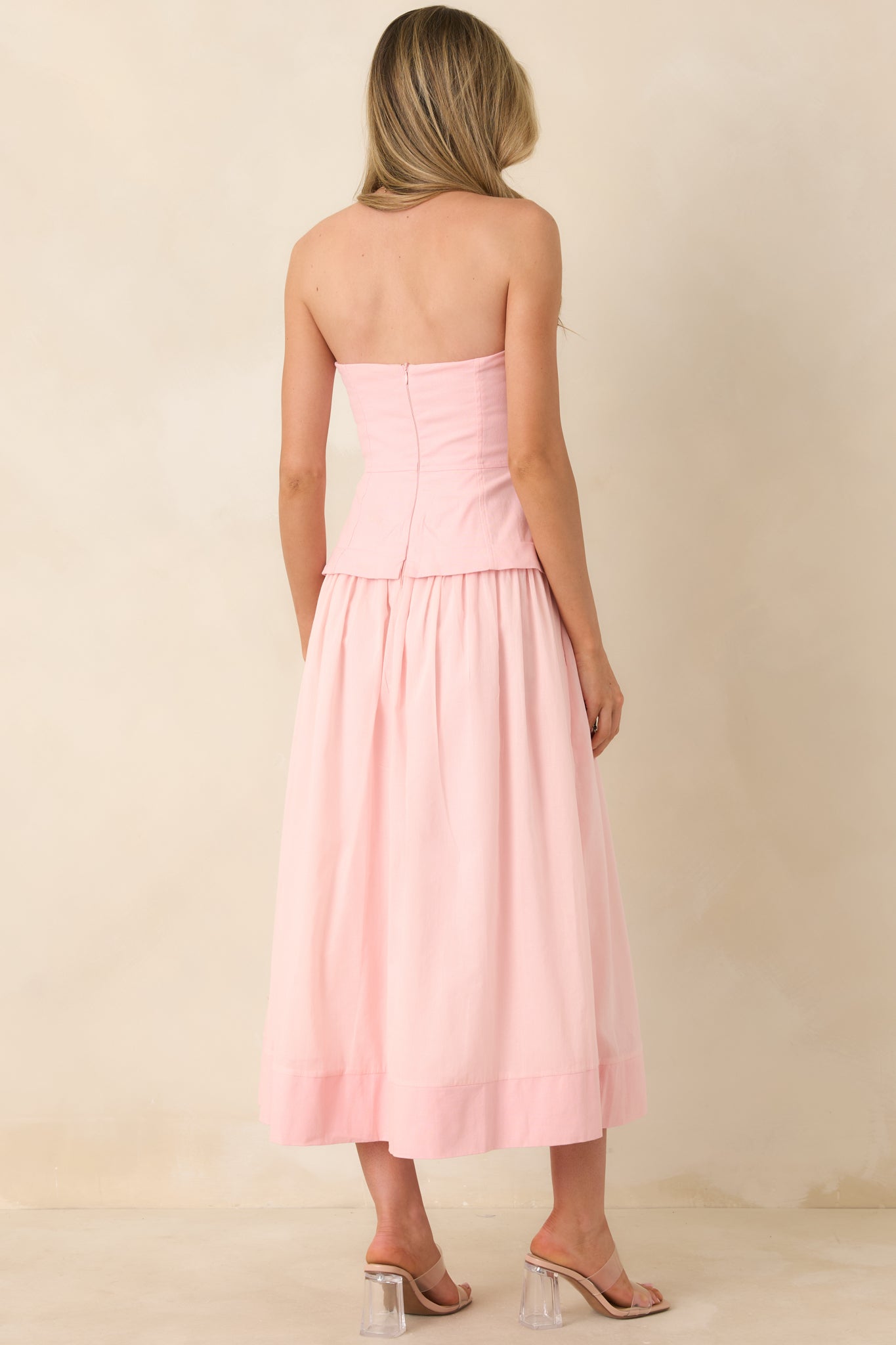 Rear view of the pink midi dress featuring a concealed zipper closure, adjustable straps, and the gathered skirt extending from the fitted bustier bodice.