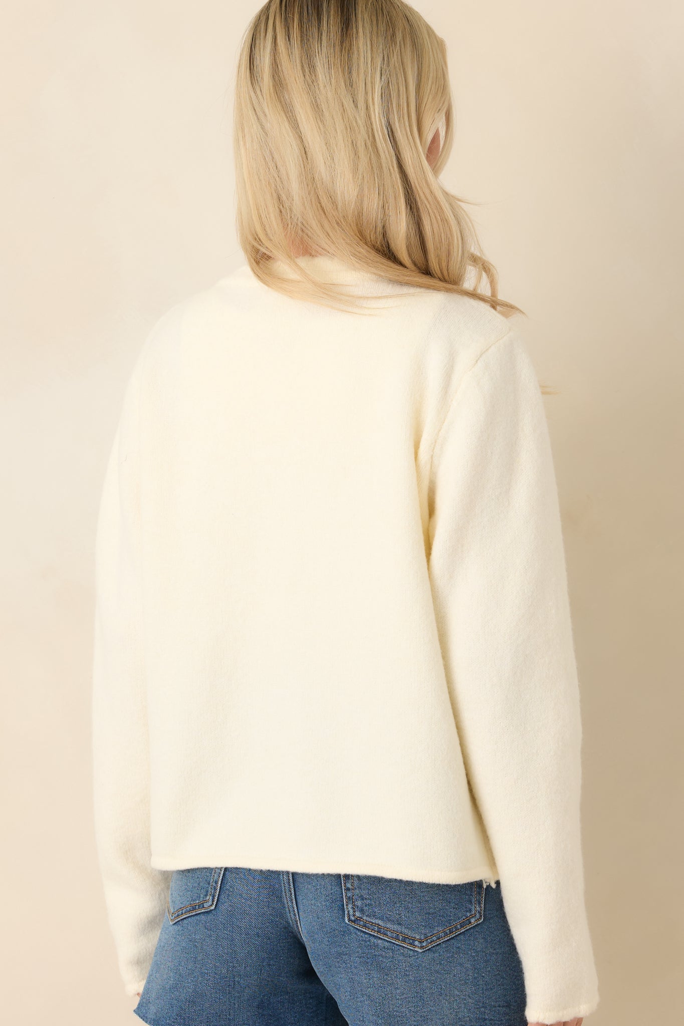 Back view of the ivory cardigan featuring long sleeves and scalloped hem along the back.