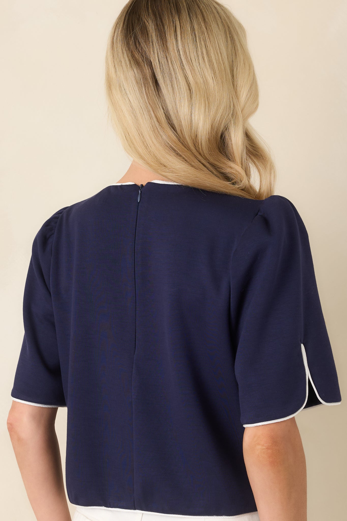 Back view of the navy top showing the puff sleeve shape, smooth fabric, and refined piping along the hem and shoulders.