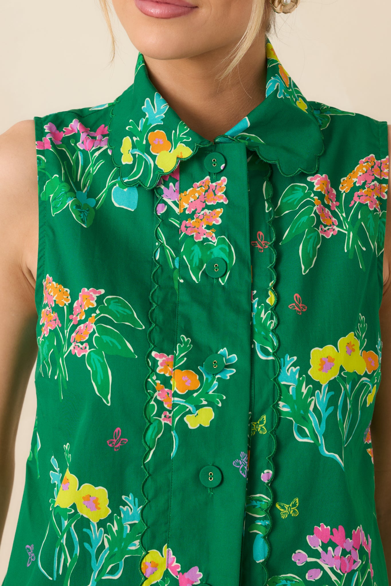 Close-up of cotton fabric showing green floral print, scalloped trim, and button-front detailing.
