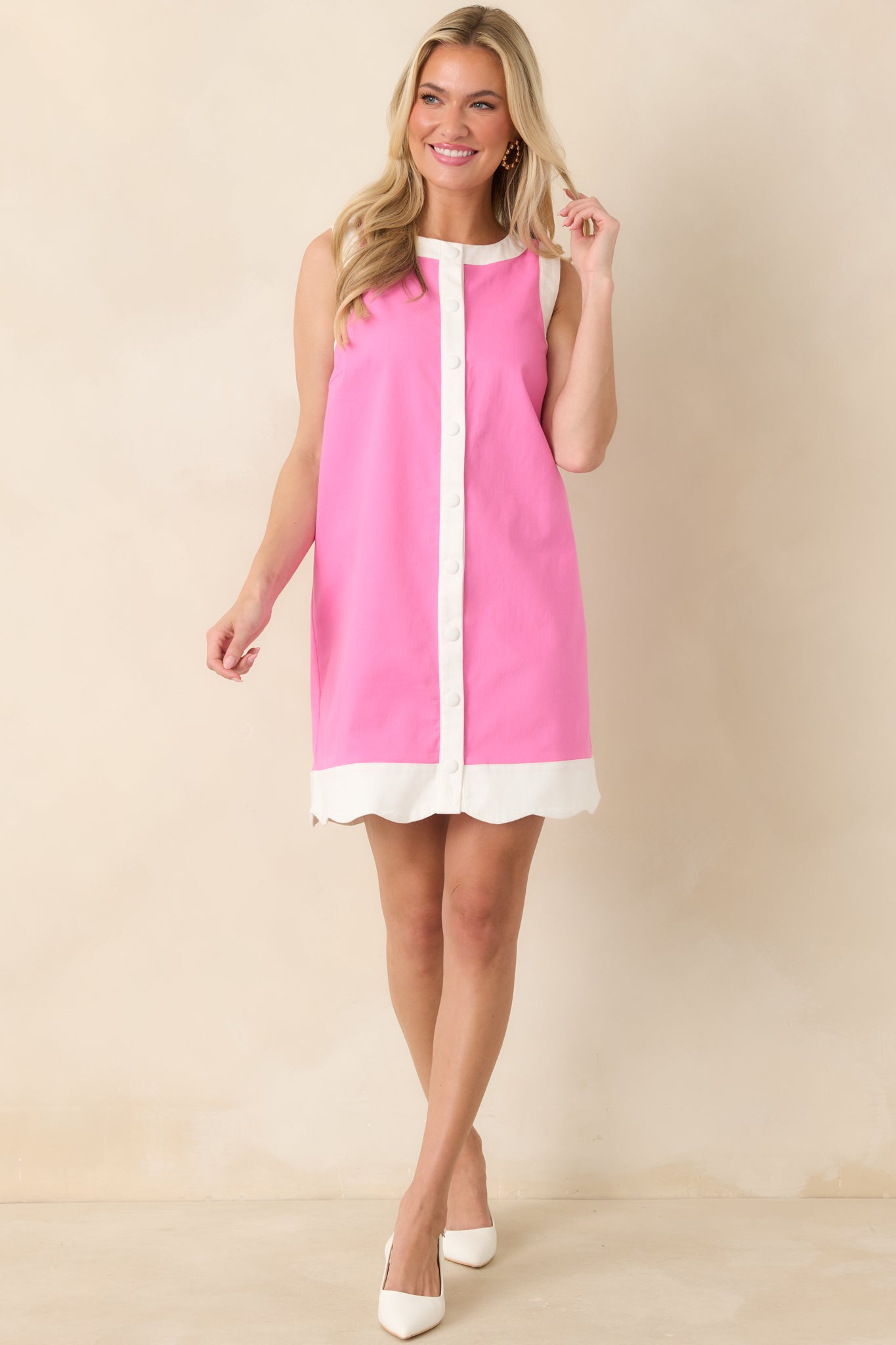 Pink cotton sleeveless mini dress with contrast trim along the neckline, arm openings, and hem, featuring a vertical placket with functional snap buttons down the front.
