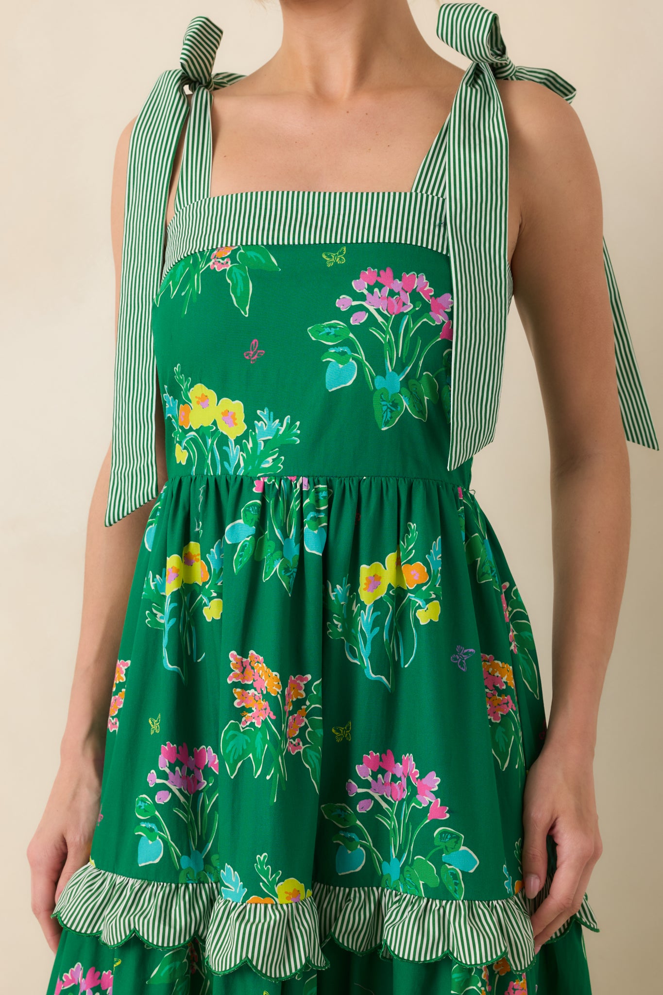 Close-up of tiered skirt showing scalloped striped trim, floral print, and adjustable shoulder tie detail.