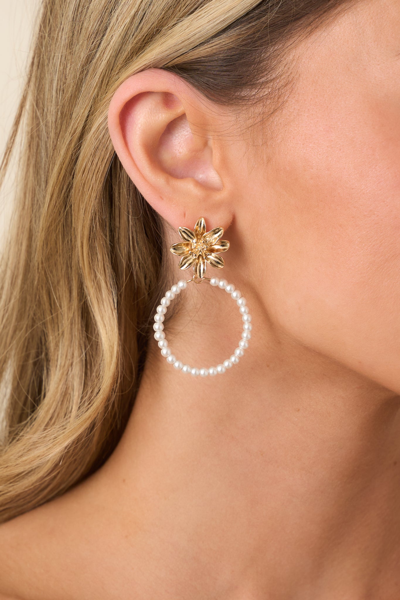 Close-up view of gold sculpted petals and delicate pearl beading, emphasizing the contrast between the structured floral stud and airy hoop.