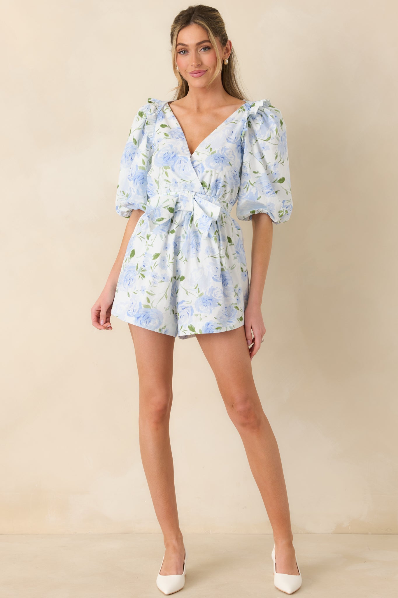 Full-length front view of the blue floral romper highlighting the V-neckline, puff sleeves, and wrap-style bodice.