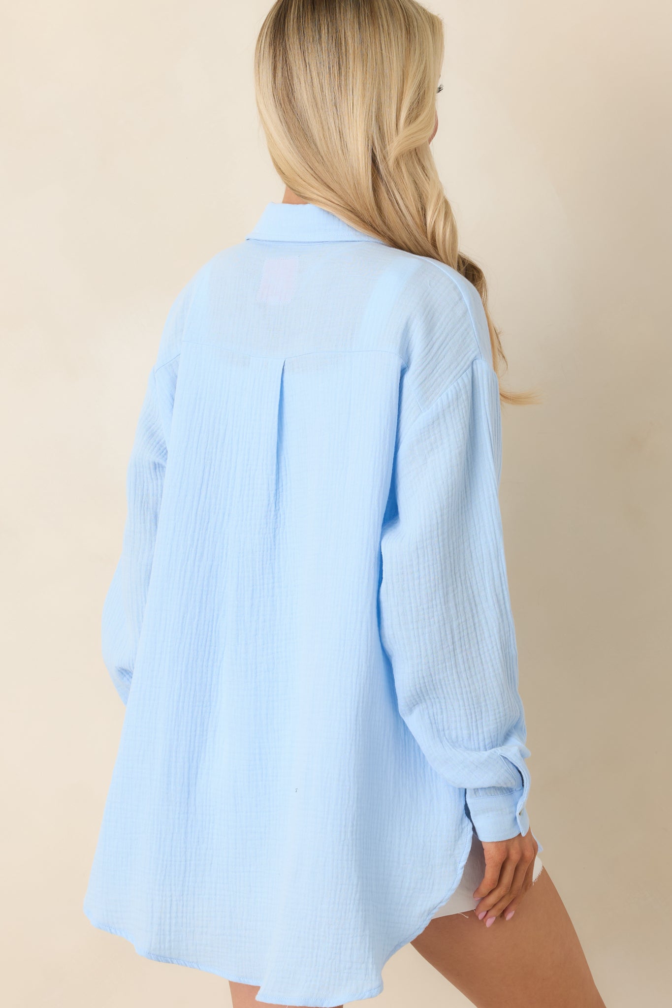 Rear view of blue cotton button-up featuring relaxed oversized fit, long sleeves, and high-low hemline.