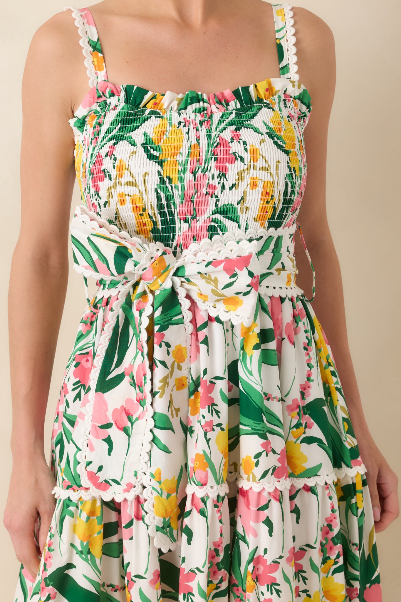 Close-up of floral cotton fabric highlighting scalloped trim, smocked bodice texture, and bow tie detail at waist.