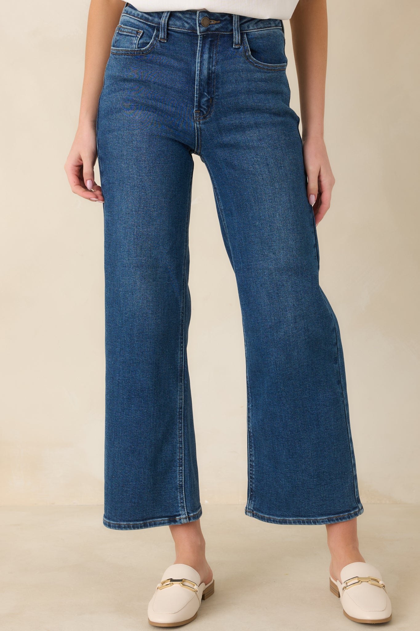 Cropped front view of dark wash jeans emphasizing the waistband, belt loops, and button-zipper closure.
