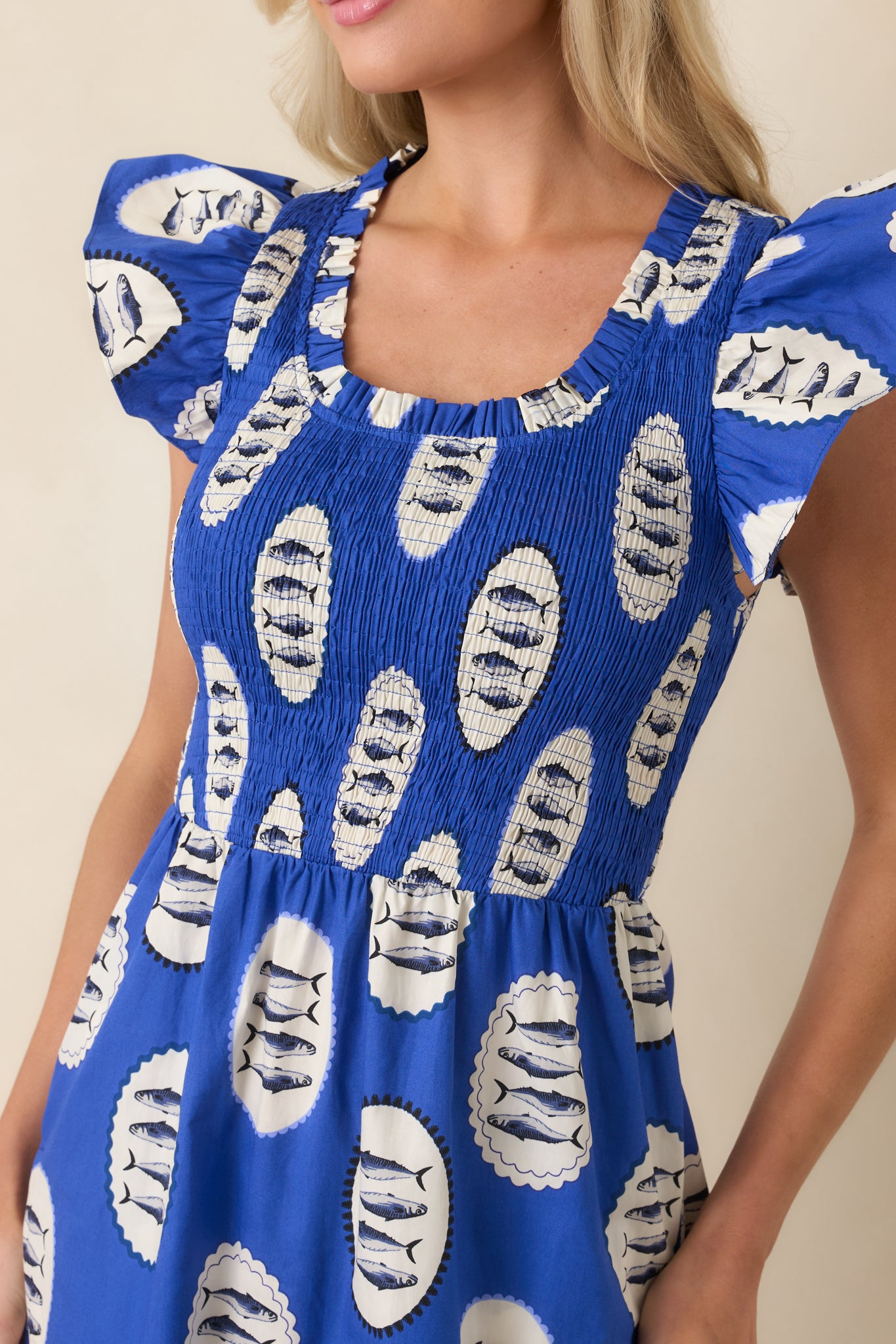 Detailed view of the royal blue cotton fabric highlighting the playful fish print, textured smocked bodice, and the delicate flutter sleeve trim.