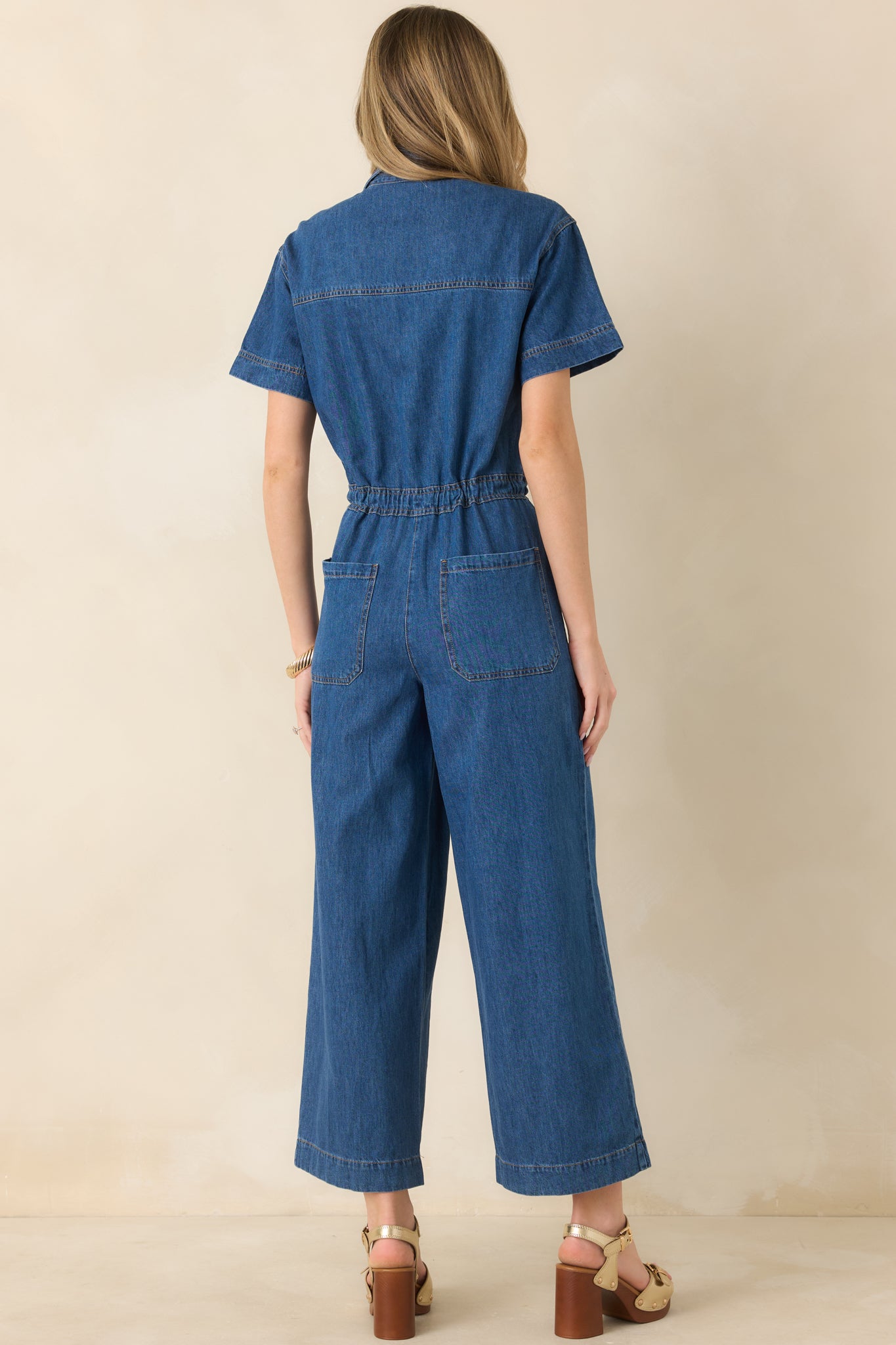 Back view of dark wash denim jumpsuit with relaxed short sleeves, cropped wide-leg silhouette, and functional patch pockets.