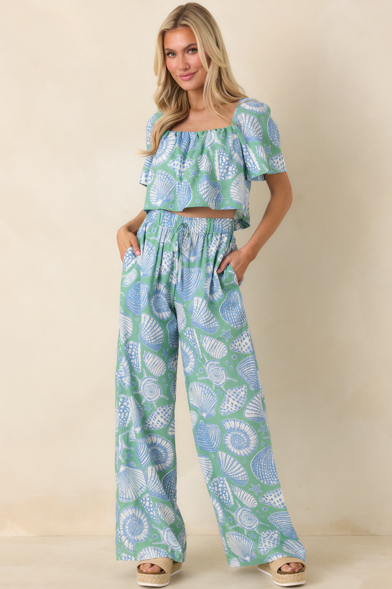 Seaglass green wide leg pants featuring oversized shell illustrations in soft blue and ivory with a relaxed, breezy silhouette.