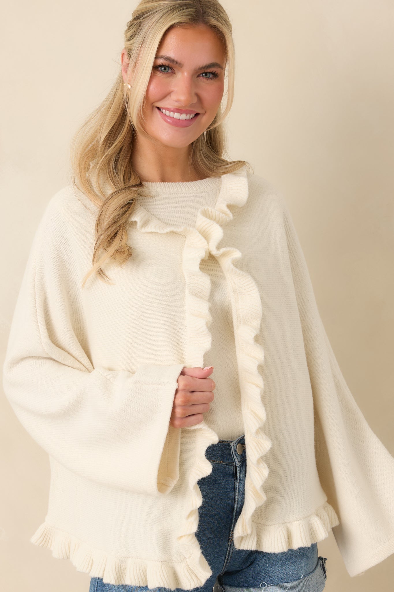 Cropped front view focusing on the ruffled neckline and open-front placket of the ivory knit cardigan.