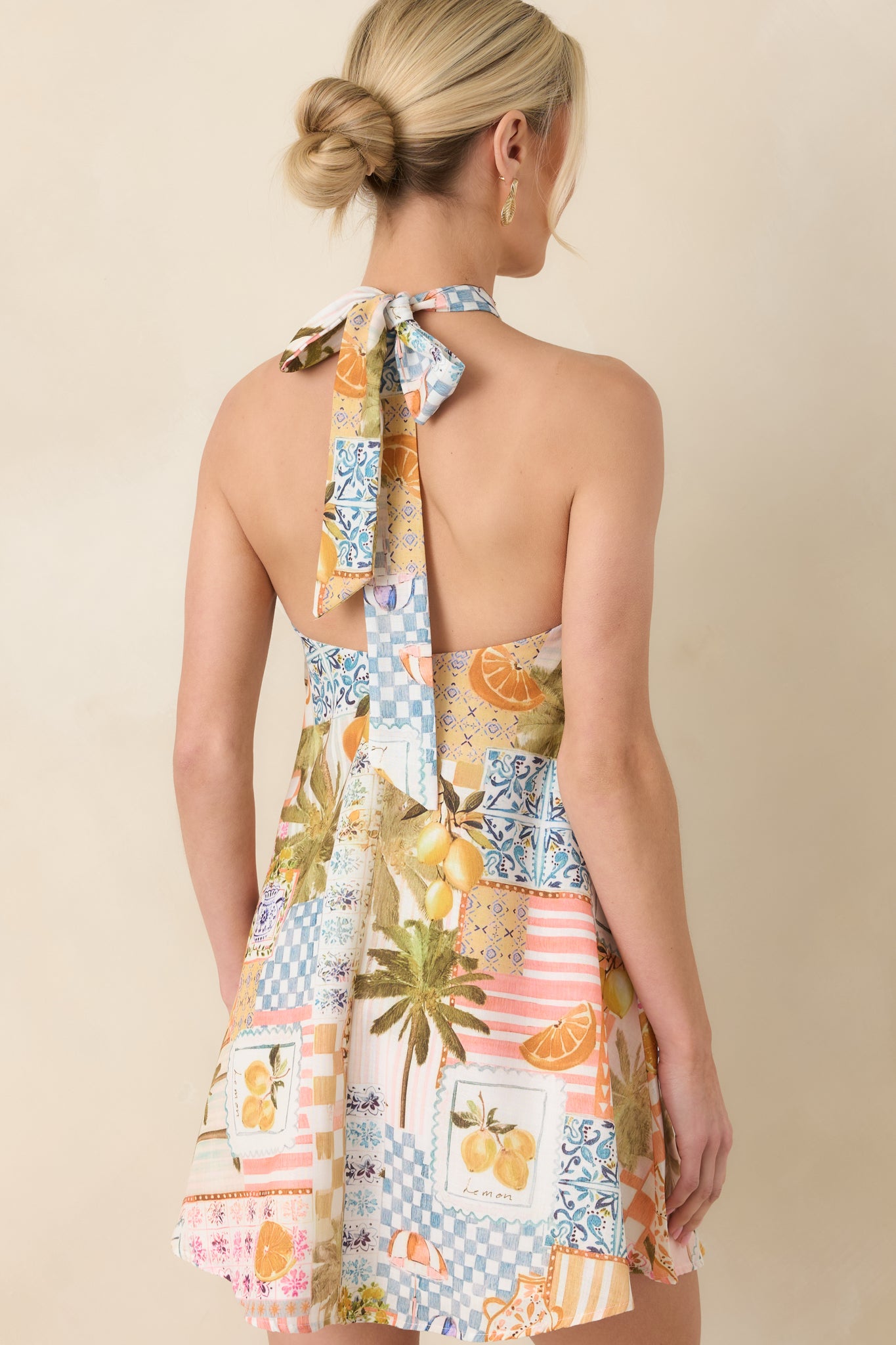 Rear view of the mini dress highlighting the halter strap design, keyhole closure, and continuous tropical patchwork print.
