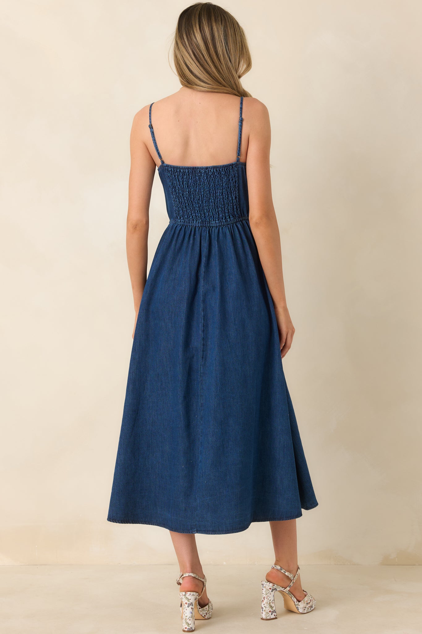 Rear view of the dark wash midi dress highlighting the smocked back panel, relaxed gathered skirt, and bow-tied shoulder straps.