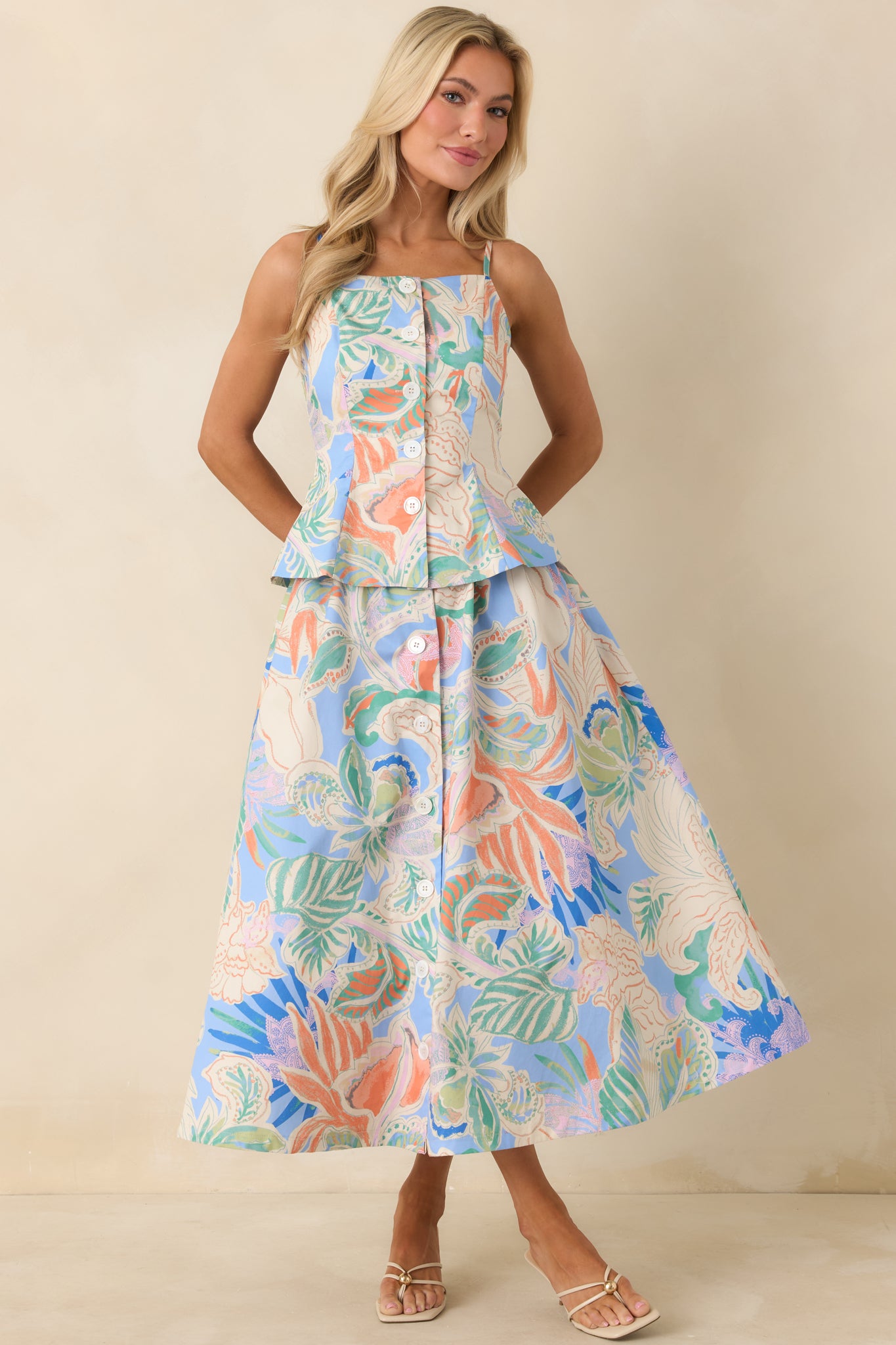 Blue multicolor sleeveless top with square neckline, front button closure, fitted bodice, and subtle peplum hem.