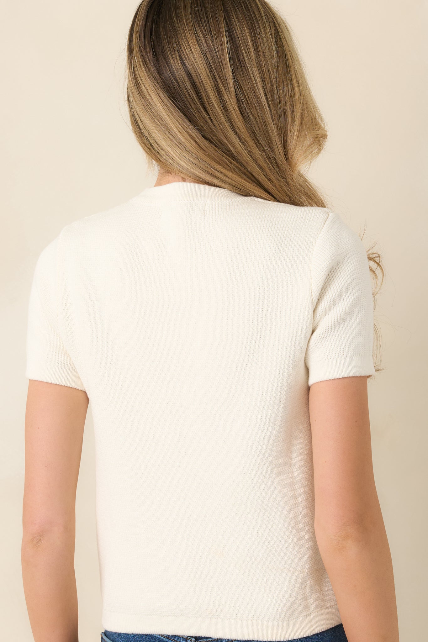 Rear view of the ivory sweater displaying the short sleeves and smooth knit finish.