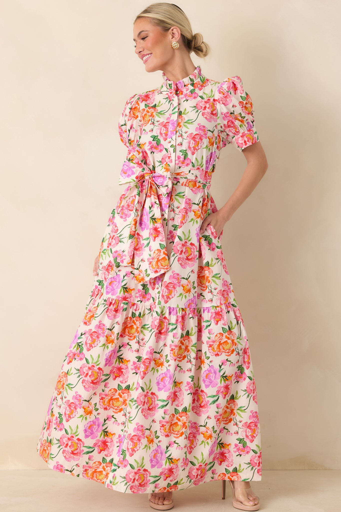 Vibrant floral cotton maxi featuring a high ruffled neckline, puffed sleeves, cinched waist with tie, and a gracefully tiered skirt.