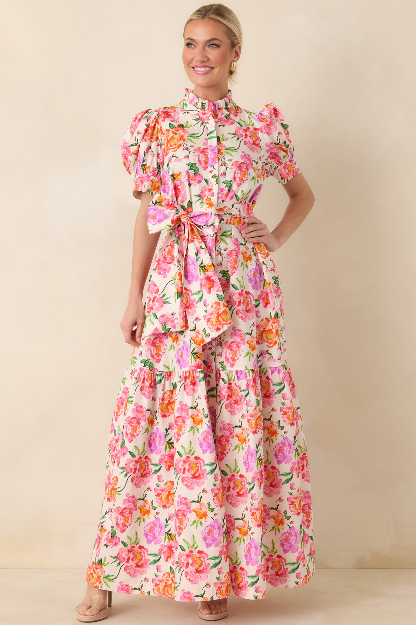 Multi floral pink maxi dress designed with puff sleeves, ruffle-accented neckline, adjustable waist tie, and a flowing tiered hemline.