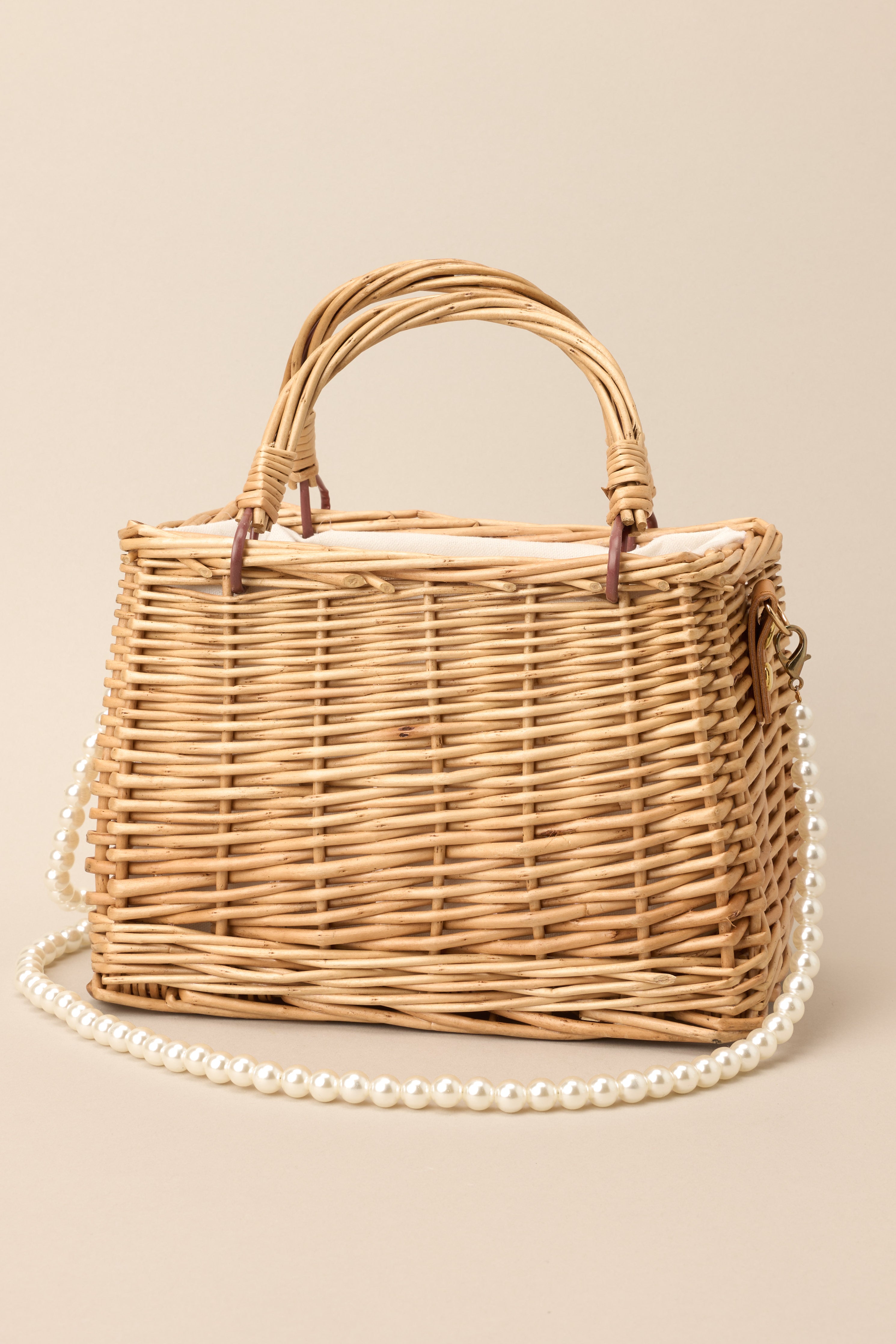 Front view of this bag that features a a wicker like design, a removable faux pearl strap, functional handles, and a drawstring closure.