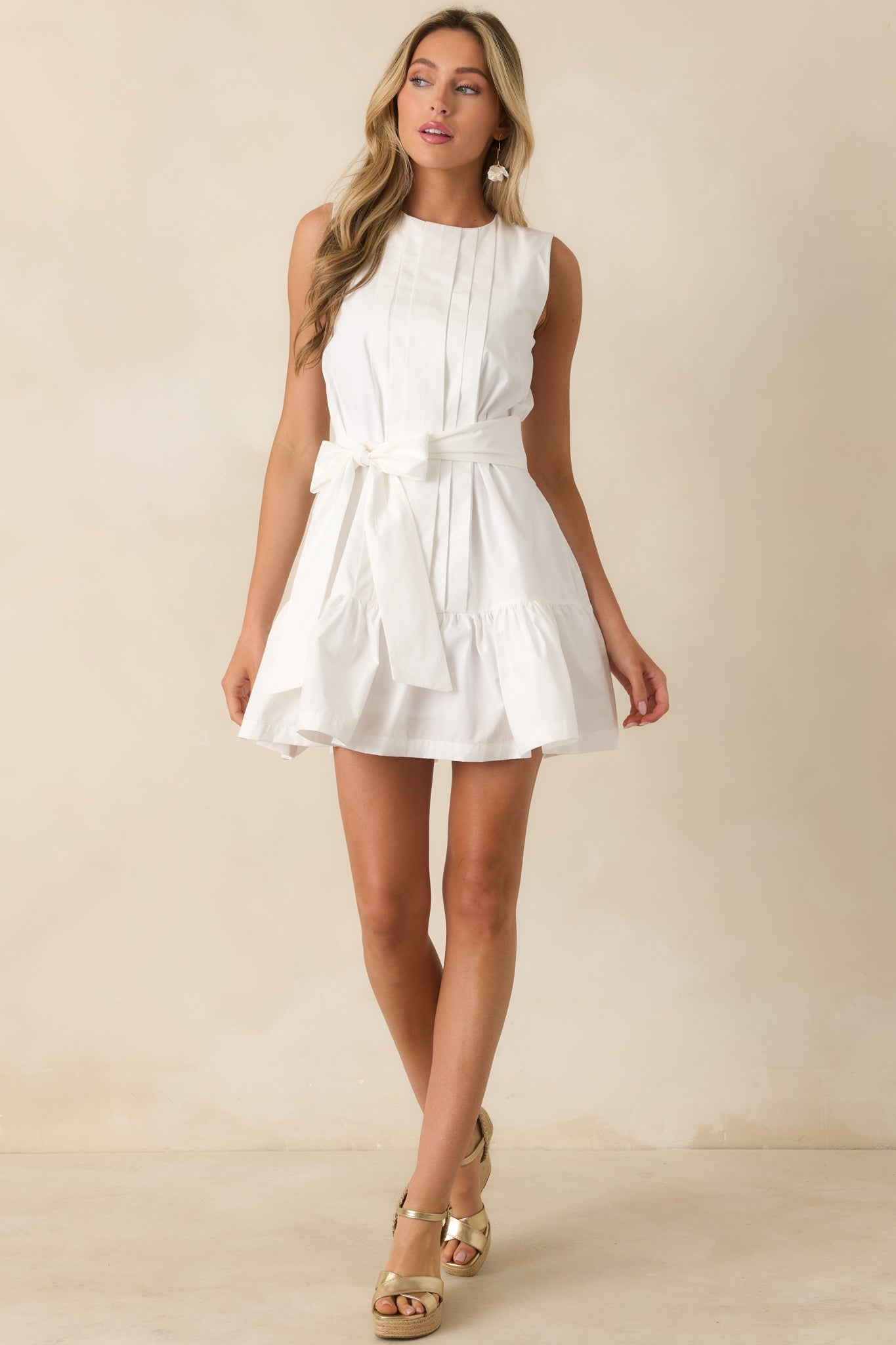 White sleeveless mini dress showcasing pleated front design, a fitted waist, and soft movement through the skirt.