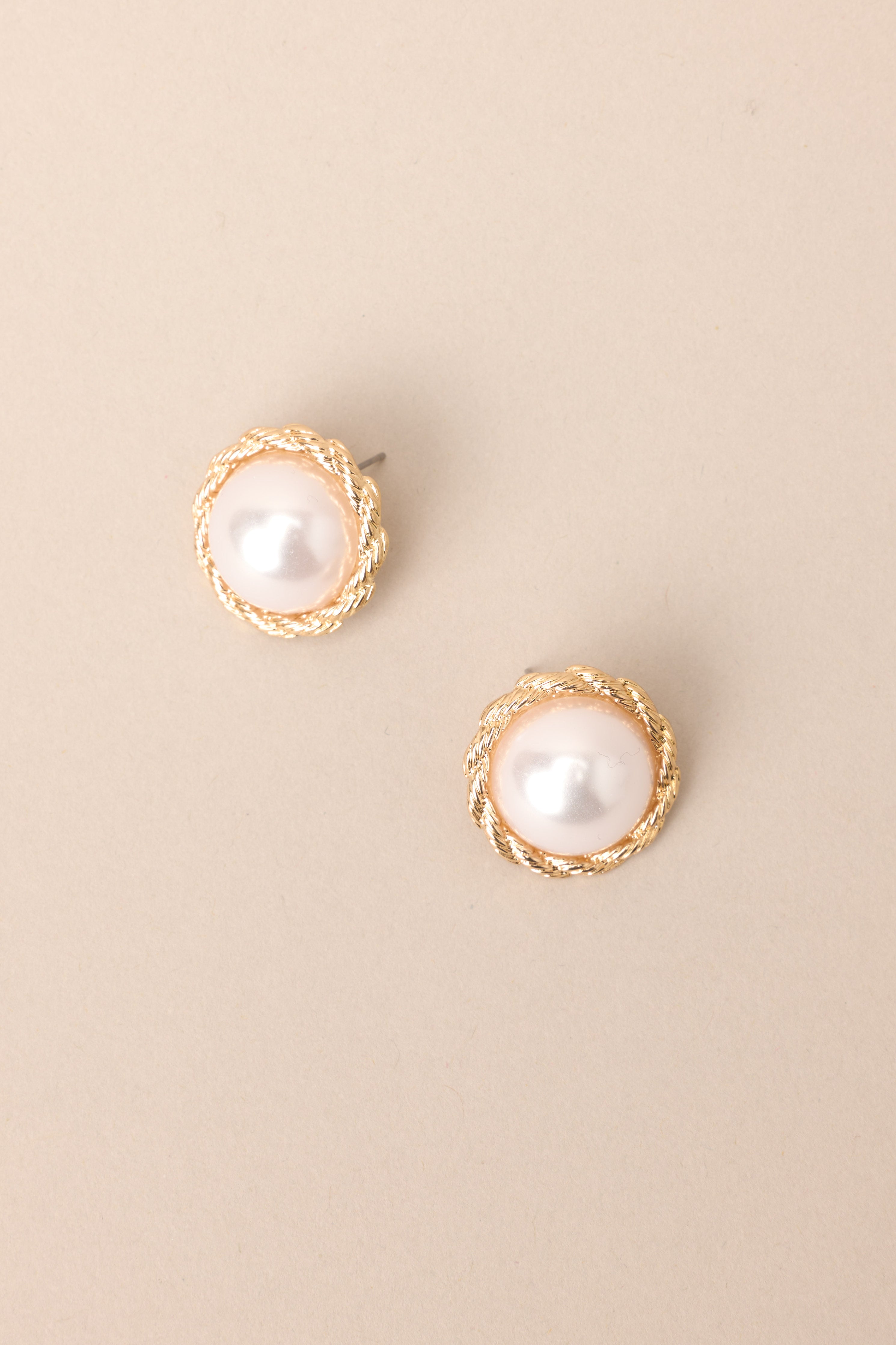 Top view of these earrings that feature a gold twisted rope-like design around a large faux pearl and a secure post backing.