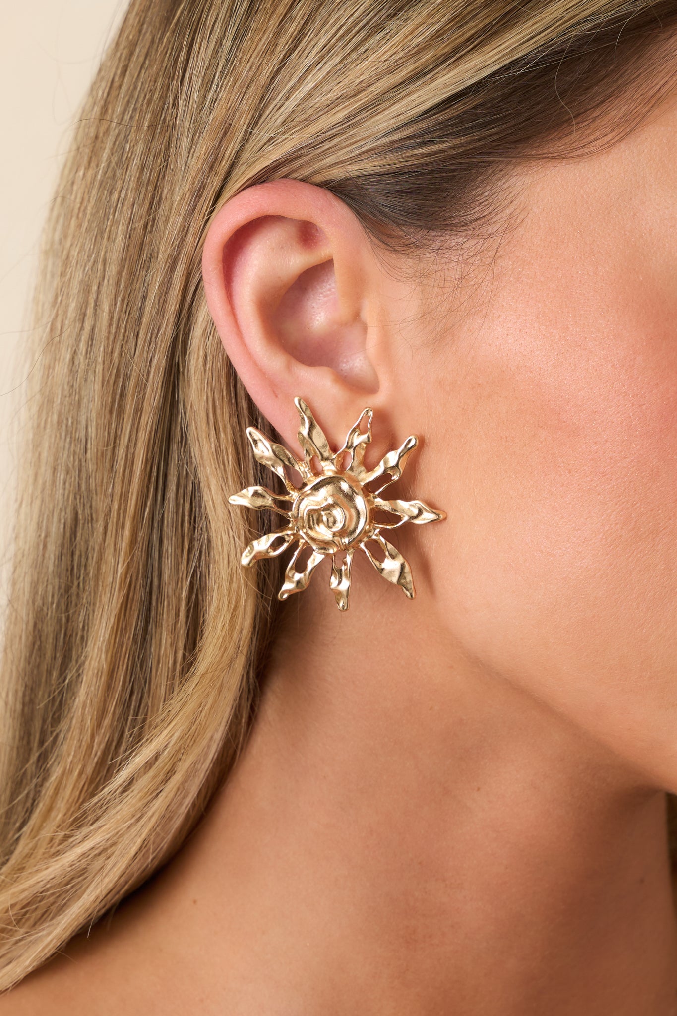 Close-up of gold sun earrings highlighting the intricate textured finish and raised swirl center with post backing.