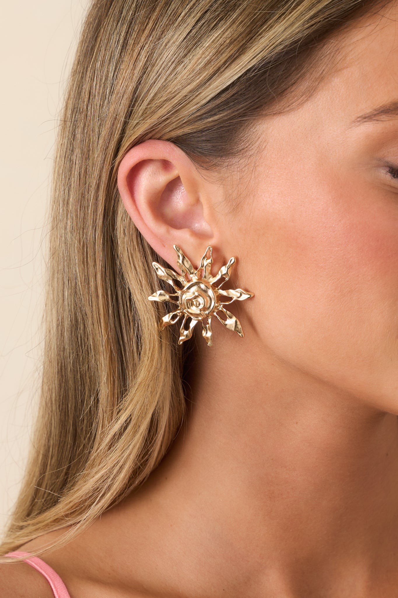 Cropped front view of gold sun-shaped earrings with textured rays and a raised swirl center.