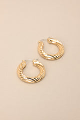 Angled overhead view of these gold hoops that feature gold hardware, a twisted design, and a lever back closure.