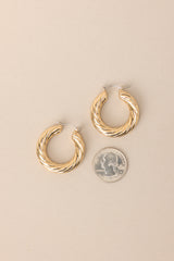 Size comparison of these gold hoops that feature gold hardware, a twisted design, and a lever back closure.
