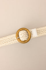 Close up view of this belt that features a woven material and a circular wooden buckle.