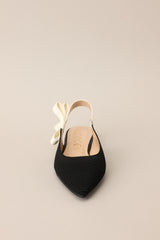 Front view of these shoes that feature a pointed toe, a textured material, a contrasting elastic strap around the back of the heel, and a subtle bow detail.