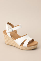 Angled front view of these espadrille sandals with white straps over the top, ankle strap with buckle closure, and wedged heel.