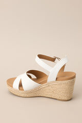 Back view of these espadrille sandals with white straps over the top, ankle strap with buckle closure, and wedged heel.