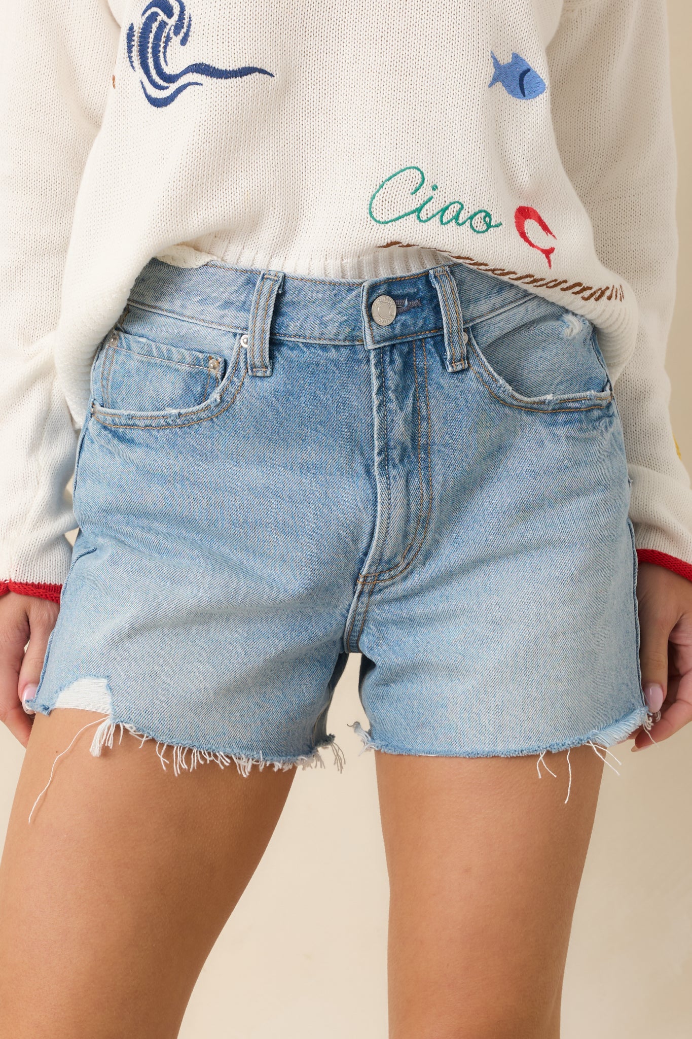 Close view of high-rise waistband and button front closure on light wash denim shorts.