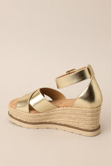 Inner-side view of these sandals that feature a rounded toe, gold hardware, crossed straps over the top of the foot, an ankle strap with a classic buckle closure, and an espadrille wedged platform.