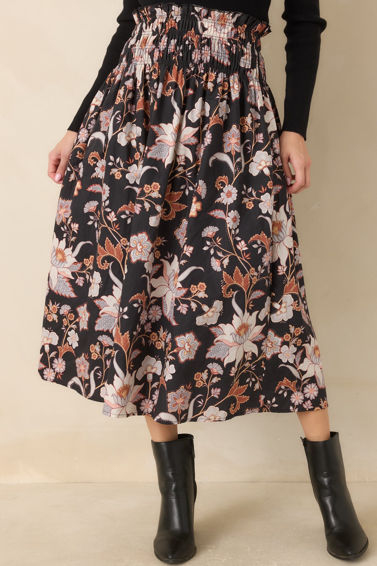 Gathered cotton creates fullness through the black midi skirt, showcasing its ivory, blush, rust, and periwinkle floral pattern.