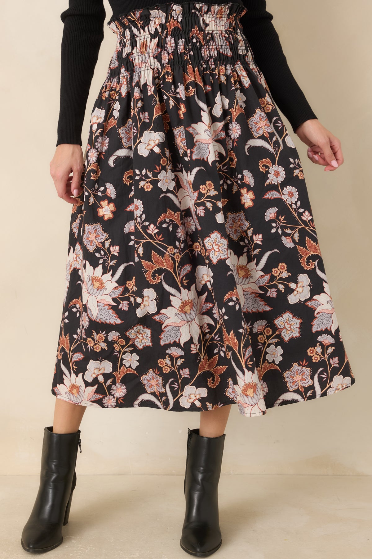 Ivory, blush, rust, and periwinkle blossoms stand out against the black cotton skirt, with gathered fabric adding soft volume below the waist.