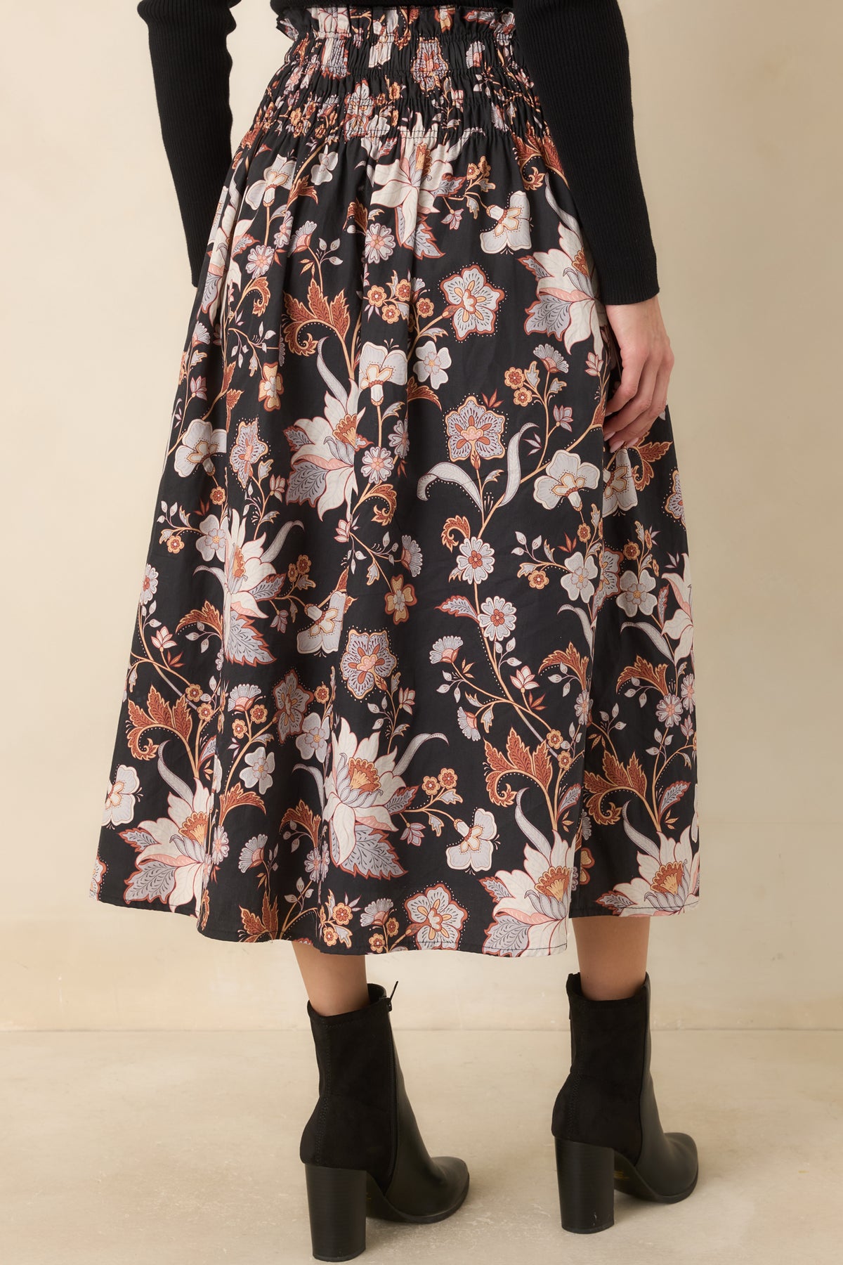 Rear view of the black floral midi skirt featuring a wide smocked waistband, gathered cotton fabric, and a flowing A-line shape.