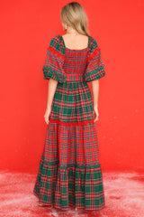 Back view of  this dress that features a square neckline, puff sleeves with elastic cuffs, a fully smocked bust, a self-tie belt at the waist, and a long, exaggerated skirt with alternating plaid patterns. 