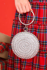 This silver bag features silver hardware, rhinestone and jewel detailing, a circular handle, an optional chain strap, and a snap closure.