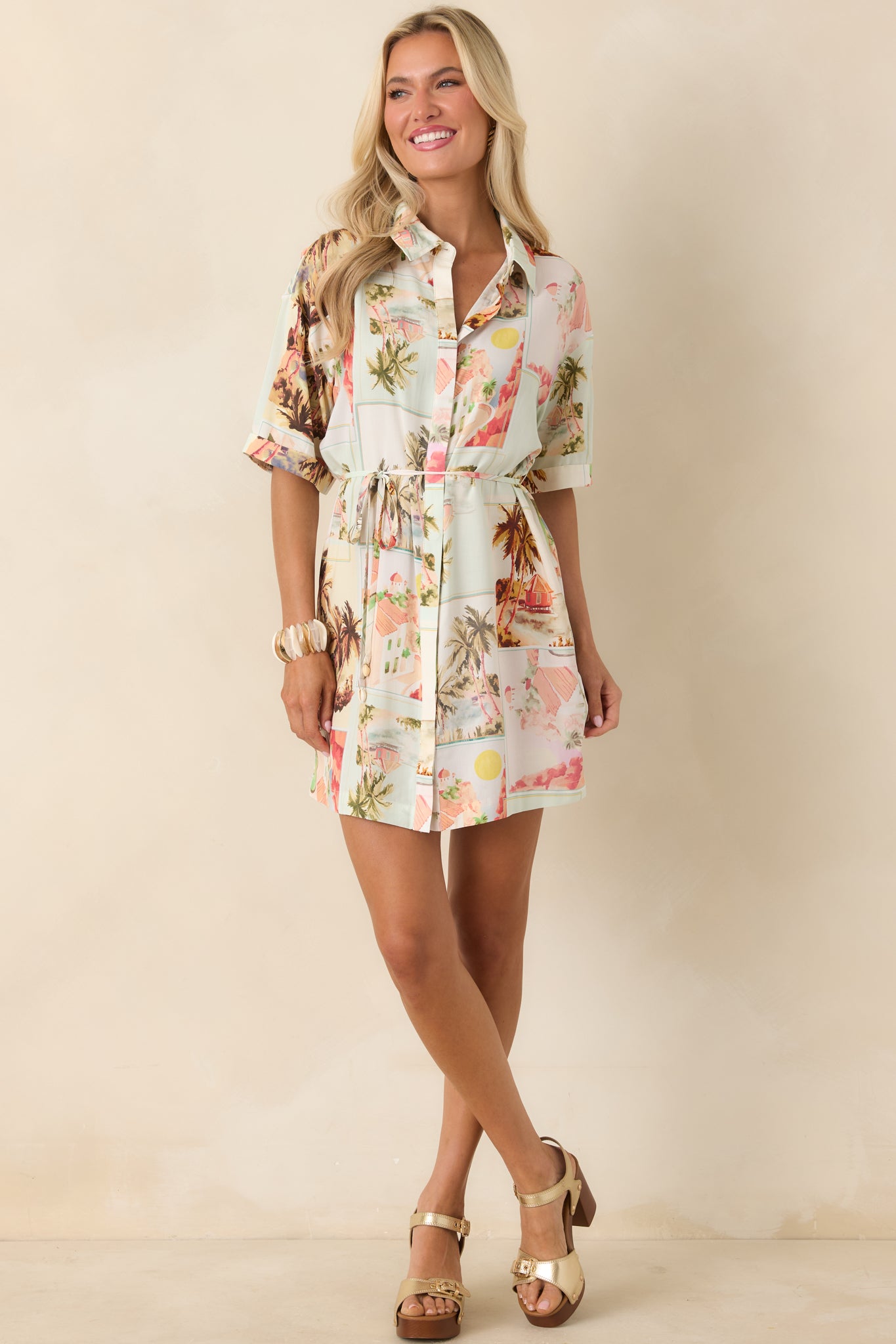 Multi-color postcard print mini shirtdress with palm tree motifs, designed with a relaxed silhouette, collared neckline, and belted waist
