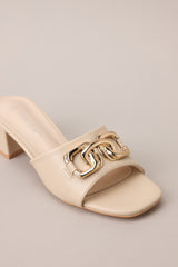 Angled front view of these heels that feature a square toe, a slide on design, a strap across the top of the foot, gold hardware, and a thick short heel.