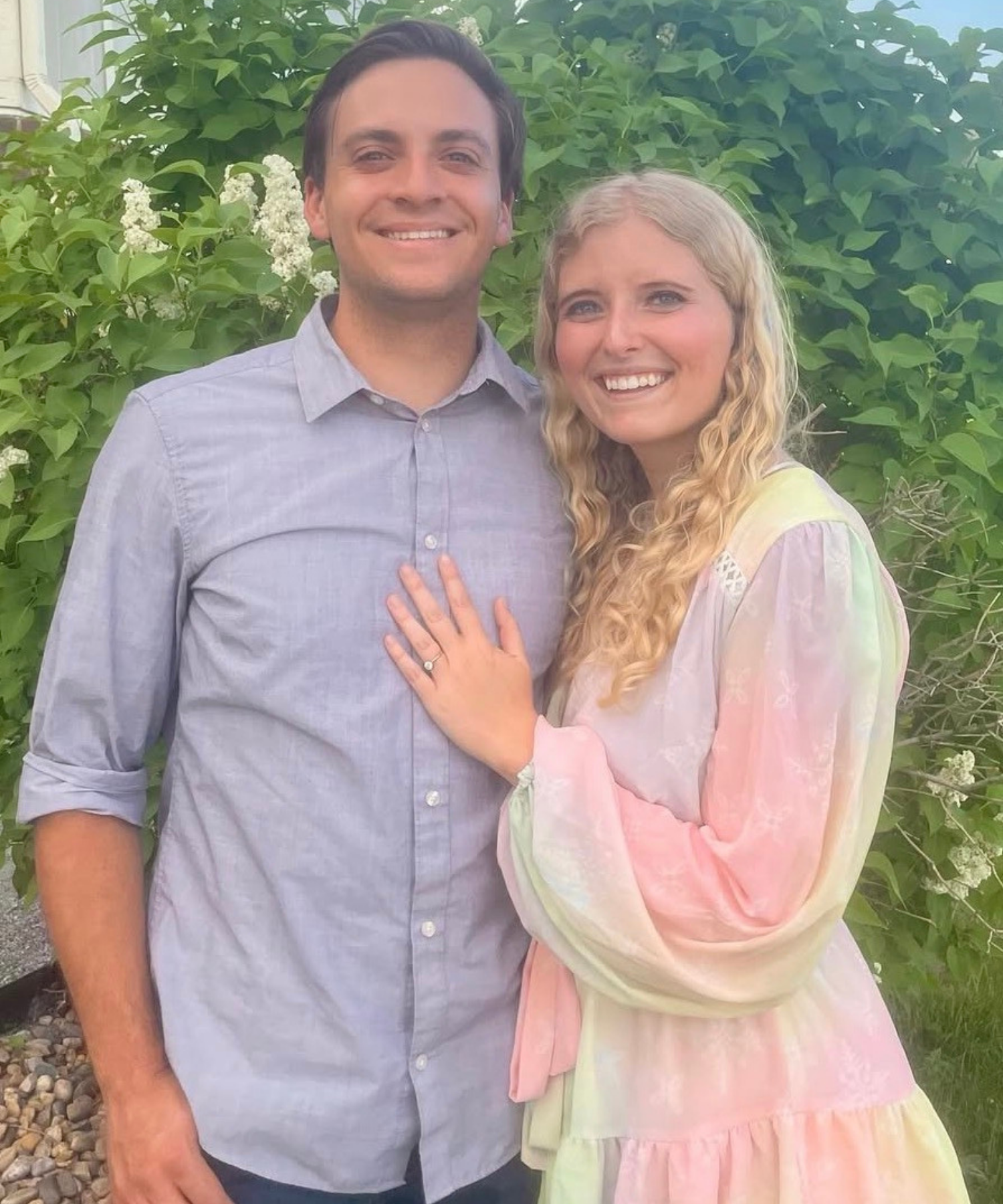 Man and woman standing together outdoors with greenery in the background.